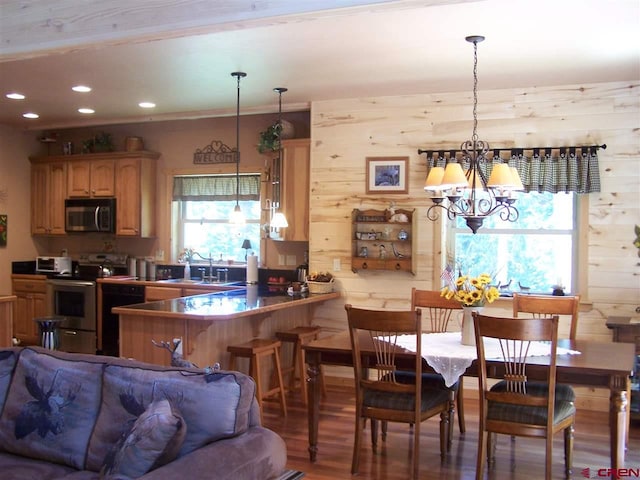 kitchen featuring wooden walls, a sink, appliances with stainless steel finishes, pendant lighting, and a notable chandelier