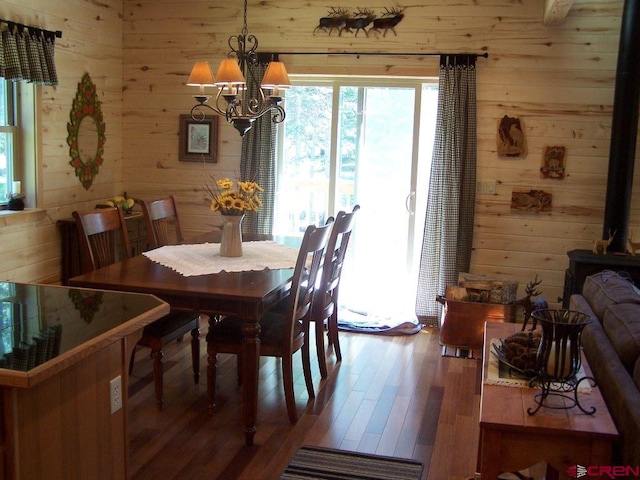 dining space with a wood stove, a notable chandelier, wood finished floors, and wood walls