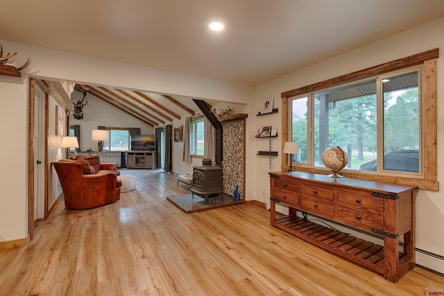 living area with a wood stove, a baseboard heating unit, light wood-style floors, baseboards, and lofted ceiling with beams