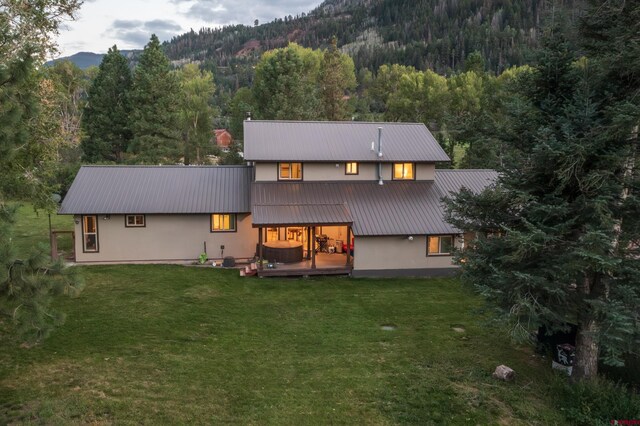 rear view of house featuring stucco siding, a yard, a wooded view, and metal roof