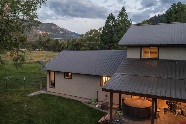 back of house featuring fence, a yard, stucco siding, a mountain view, and metal roof