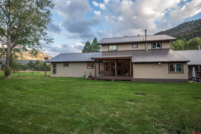 back of property featuring stucco siding, a mountain view, a yard, and metal roof