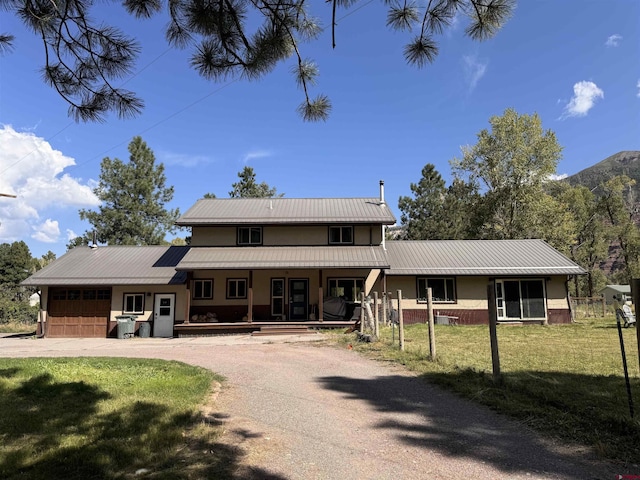 traditional home featuring an attached garage, driveway, covered porch, a front yard, and metal roof
