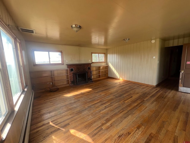 unfurnished living room featuring a wealth of natural light, wood-type flooring, and a brick fireplace