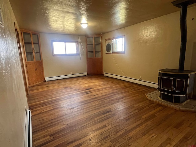 basement with a baseboard radiator, a wood stove, and dark hardwood / wood-style floors