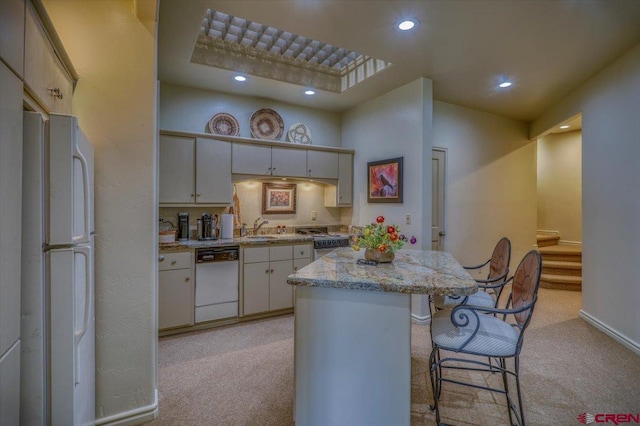 kitchen featuring light carpet, white appliances, a breakfast bar area, and white cabinets