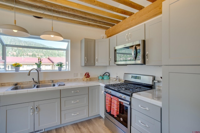 kitchen featuring decorative light fixtures, appliances with stainless steel finishes, light hardwood / wood-style floors, tile counters, and sink