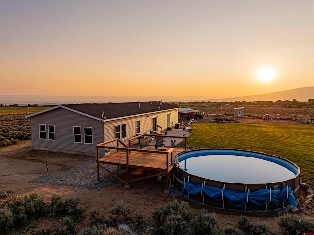 back house at dusk featuring a lawn and a swimming pool side deck