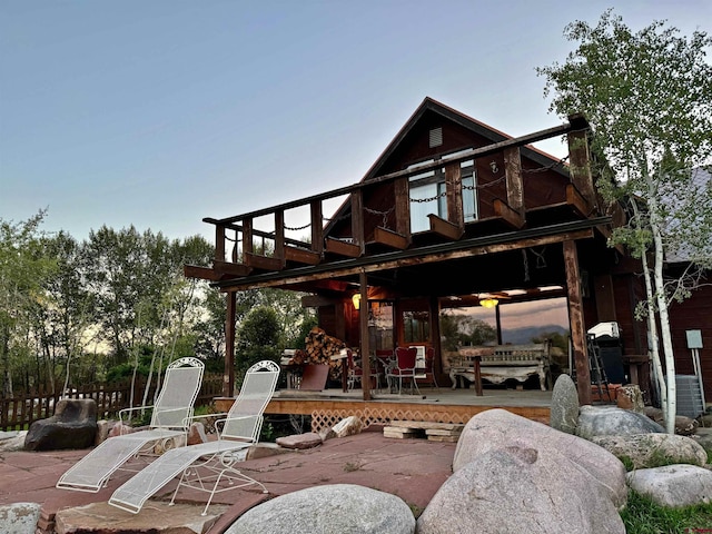 back house at dusk featuring a wooden deck and a patio