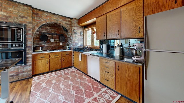 kitchen with brick wall, black appliances, and light hardwood / wood-style floors