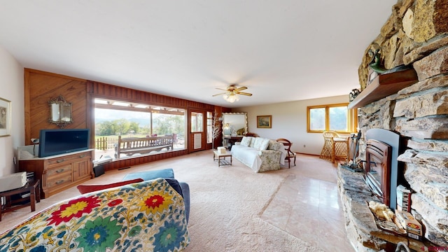 carpeted living room featuring ceiling fan, a stone fireplace, and wooden walls