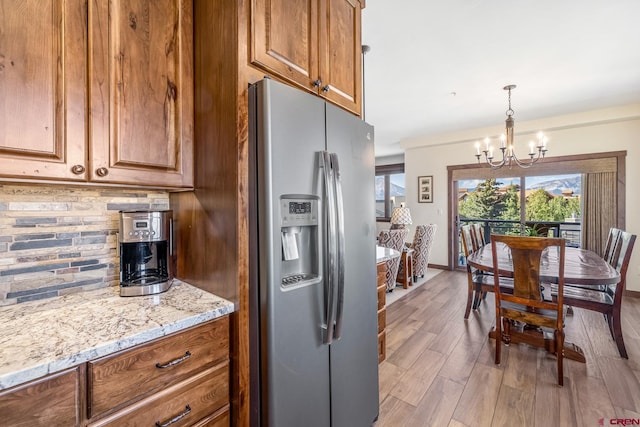 kitchen featuring stainless steel refrigerator with ice dispenser, tasteful backsplash, light hardwood / wood-style flooring, and a notable chandelier