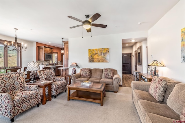 living room with sink, ceiling fan with notable chandelier, and light carpet