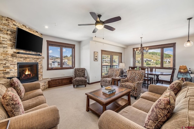 carpeted living room featuring ceiling fan with notable chandelier and a stone fireplace