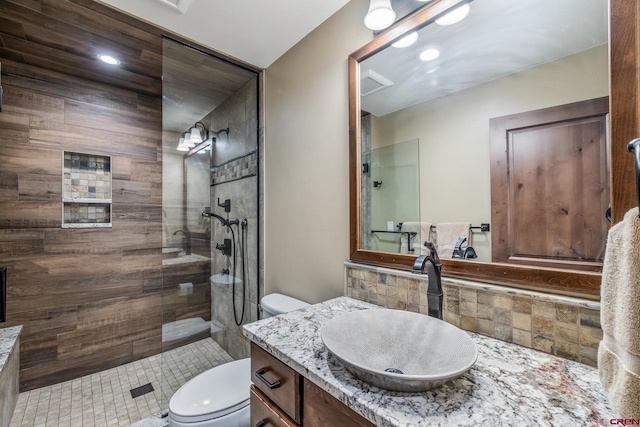 bathroom with tile patterned flooring, vanity, toilet, and a tile shower