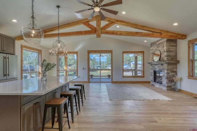 dining area featuring a healthy amount of sunlight, ceiling fan with notable chandelier, a stone fireplace, and light wood-type flooring