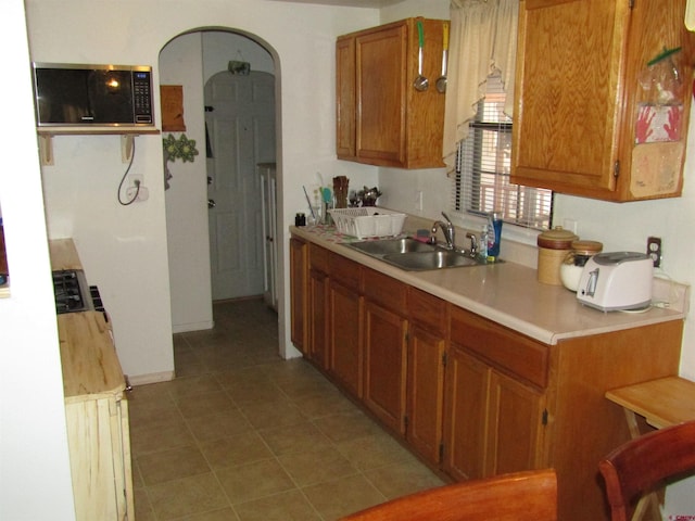 730 Washington St, Monte Vista, CO 81144 - kitchen featuring light countertops, stainless steel microwave, a sink, arched walkways, and brown cabinetry