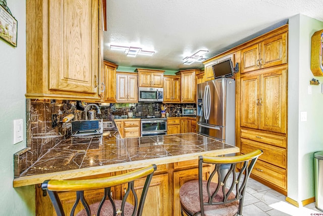 kitchen with appliances with stainless steel finishes, a textured ceiling, kitchen peninsula, and decorative backsplash