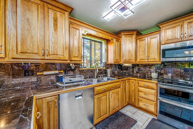 kitchen with a textured ceiling, light tile patterned floors, appliances with stainless steel finishes, sink, and decorative backsplash