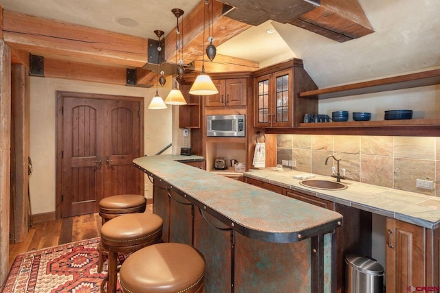 kitchen featuring dark hardwood / wood-style flooring, stainless steel microwave, decorative light fixtures, a kitchen breakfast bar, and backsplash