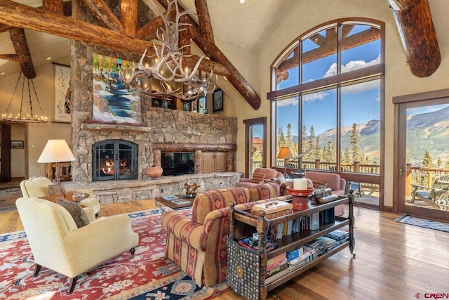 living room featuring high vaulted ceiling, a stone fireplace, hardwood / wood-style flooring, a notable chandelier, and a mountain view