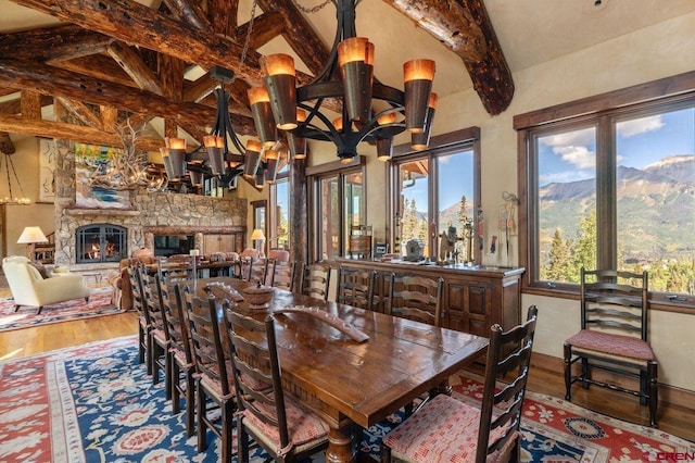 dining area featuring an inviting chandelier, a mountain view, a fireplace, vaulted ceiling with beams, and hardwood / wood-style flooring