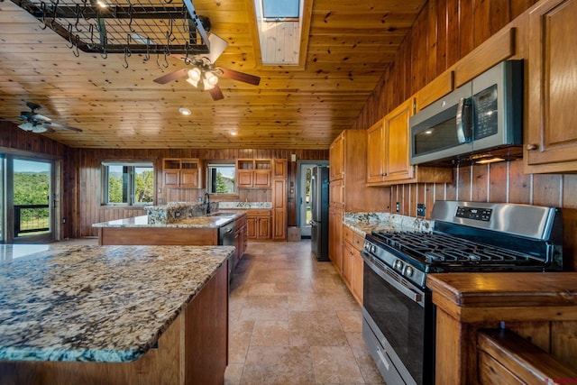 kitchen featuring appliances with stainless steel finishes, wooden walls, a center island with sink, and ceiling fan