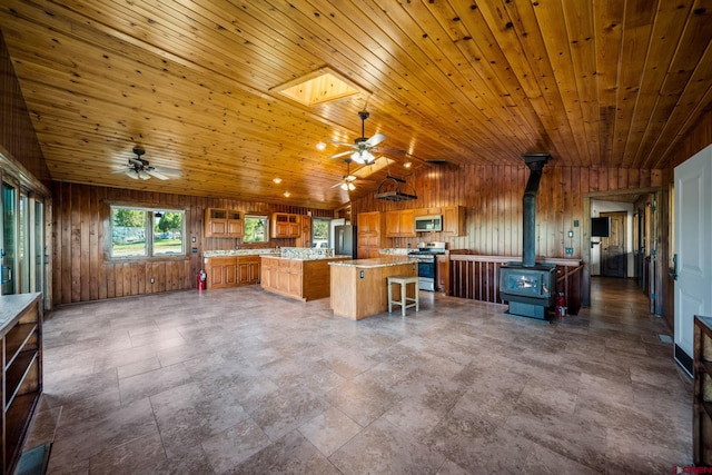 kitchen featuring vaulted ceiling, a wood stove, appliances with stainless steel finishes, wood ceiling, and ceiling fan