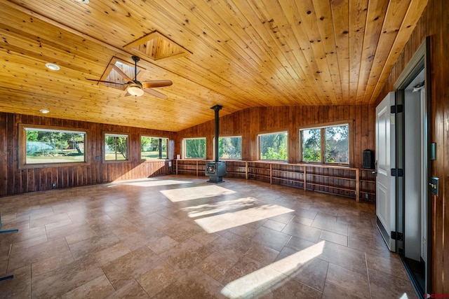 empty room featuring wood ceiling, a wood stove, vaulted ceiling with skylight, wood walls, and ceiling fan