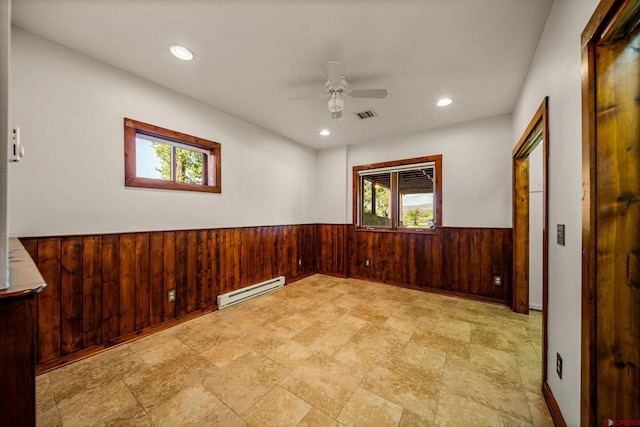 empty room with a baseboard heating unit, plenty of natural light, ceiling fan, and wood walls