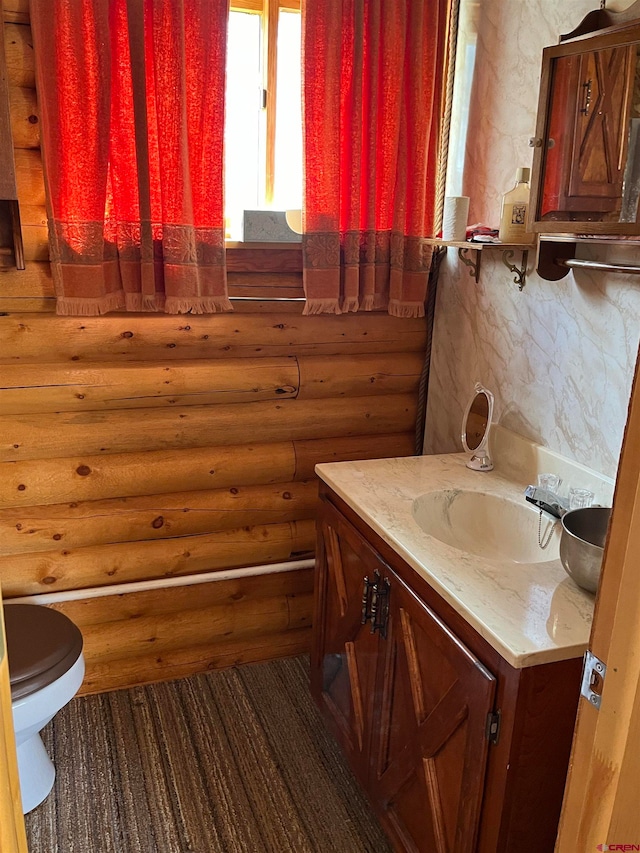 bathroom with vanity, toilet, and log walls