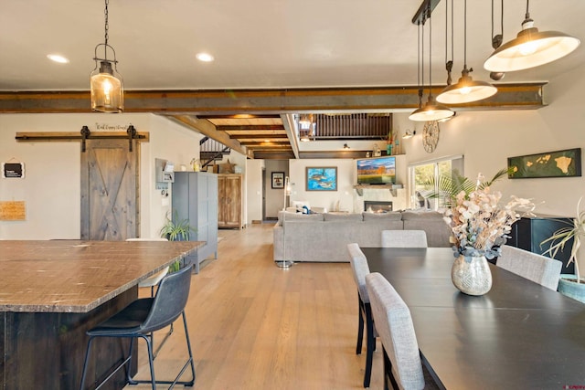 dining room with a barn door, beamed ceiling, and light hardwood / wood-style floors