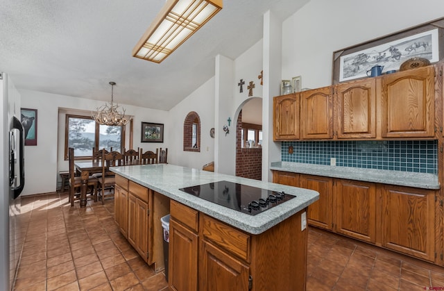 kitchen with a chandelier, black electric stovetop, a kitchen island, pendant lighting, and tasteful backsplash