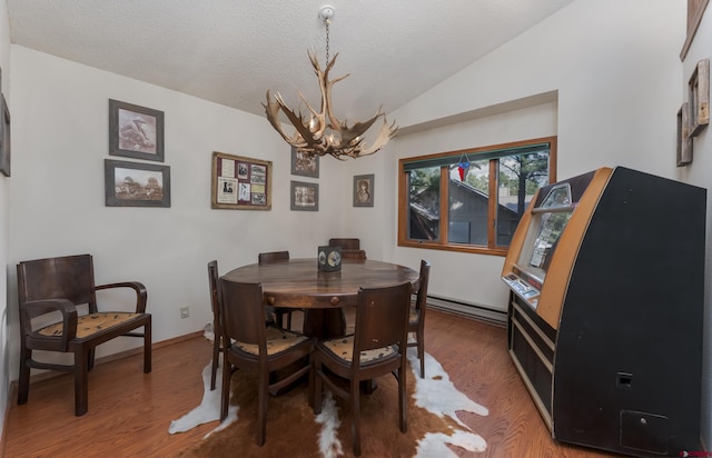 dining room featuring a textured ceiling, baseboard heating, an inviting chandelier, vaulted ceiling, and hardwood / wood-style flooring