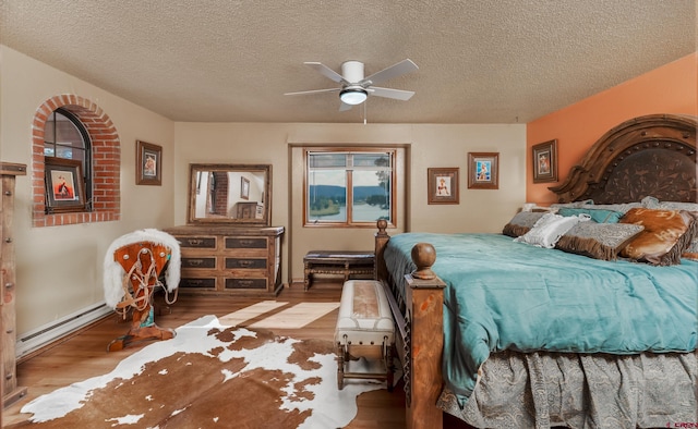 bedroom featuring a textured ceiling, baseboard heating, hardwood / wood-style floors, and ceiling fan