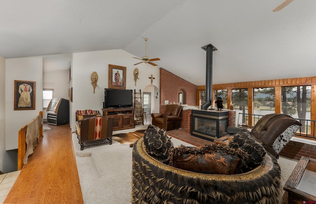 living room featuring a wood stove, ceiling fan, light wood-type flooring, and vaulted ceiling