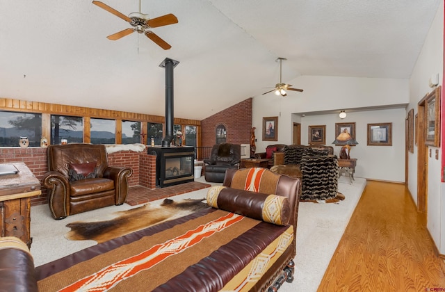 living room featuring lofted ceiling, ceiling fan, a wood stove, and light hardwood / wood-style flooring