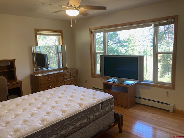 bedroom featuring multiple windows, a baseboard heating unit, and light hardwood / wood-style flooring