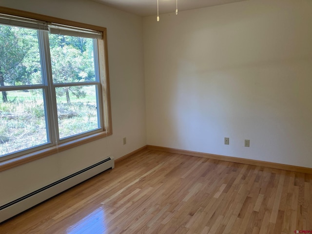 unfurnished room featuring baseboard heating, a healthy amount of sunlight, and light hardwood / wood-style floors