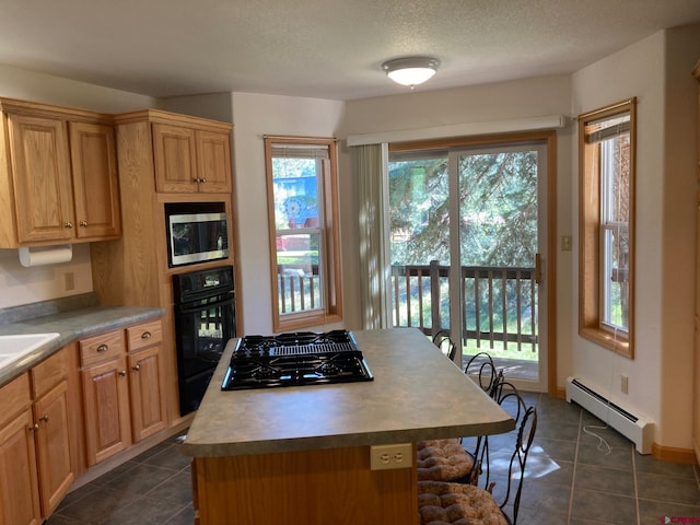 kitchen featuring dark tile patterned flooring, appliances with stainless steel finishes, a kitchen island, and baseboard heating