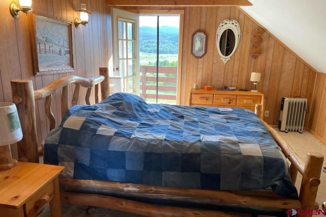 bedroom with carpet floors, wood walls, radiator, and access to exterior