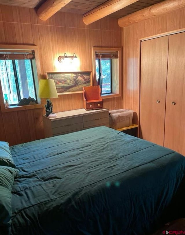 bedroom featuring wooden walls, beam ceiling, ceiling fan, and a closet