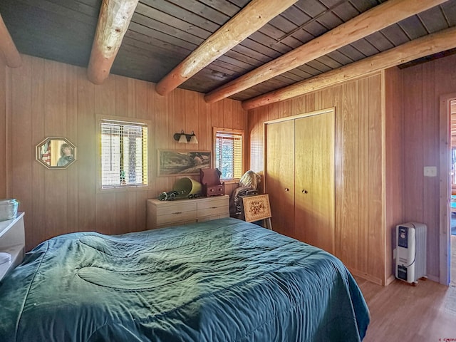 bedroom with a closet, beam ceiling, light hardwood / wood-style floors, and wood walls