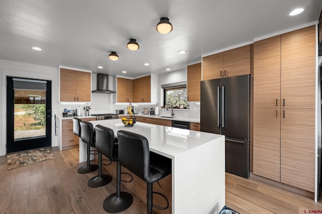 kitchen featuring a kitchen breakfast bar, stainless steel appliances, a center island, light hardwood / wood-style flooring, and wall chimney range hood