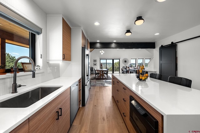 kitchen featuring appliances with stainless steel finishes, a barn door, beam ceiling, light hardwood / wood-style flooring, and sink