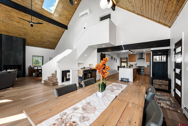 dining space featuring ceiling fan, a skylight, light wood-type flooring, high vaulted ceiling, and a fireplace