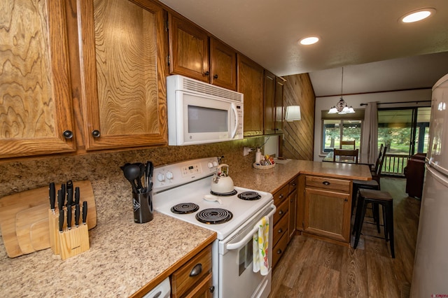 kitchen with pendant lighting, a notable chandelier, vaulted ceiling, white appliances, and dark hardwood / wood-style flooring