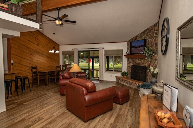 living room with ceiling fan with notable chandelier, wood-type flooring, lofted ceiling with beams, and a fireplace