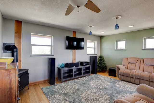 living room with ceiling fan, a textured ceiling, hardwood / wood-style floors, and a wood stove