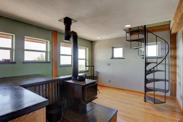 home office with light wood-type flooring, a textured ceiling, and a wood stove